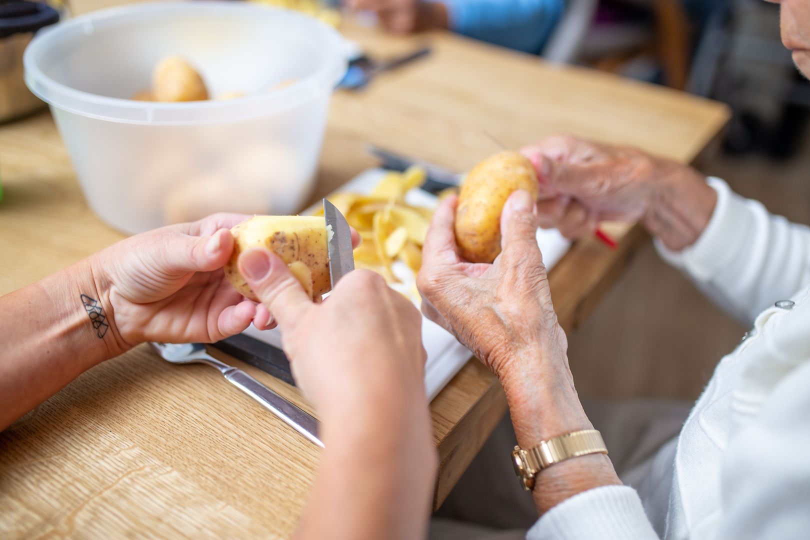 Pflegerin schält mit einer Seniorin Kartoffeln um die Feinmotorik zu stärken